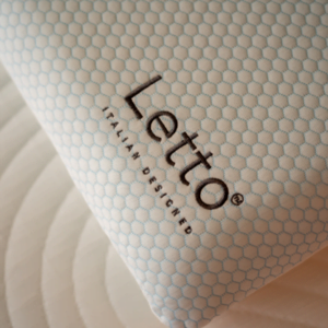 Close-up of a Letto pillow with a light blue hexagonal patterned cover, featuring the Letto logo and the words ‘Italian Designed,’ resting on a mattress with circular quilted stitching.