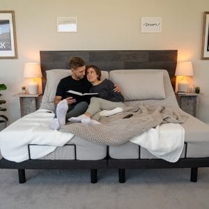 A couple smiles while reading a book on a split adjustable bed, which can help find a comfortable position for how to sleep in the heat.