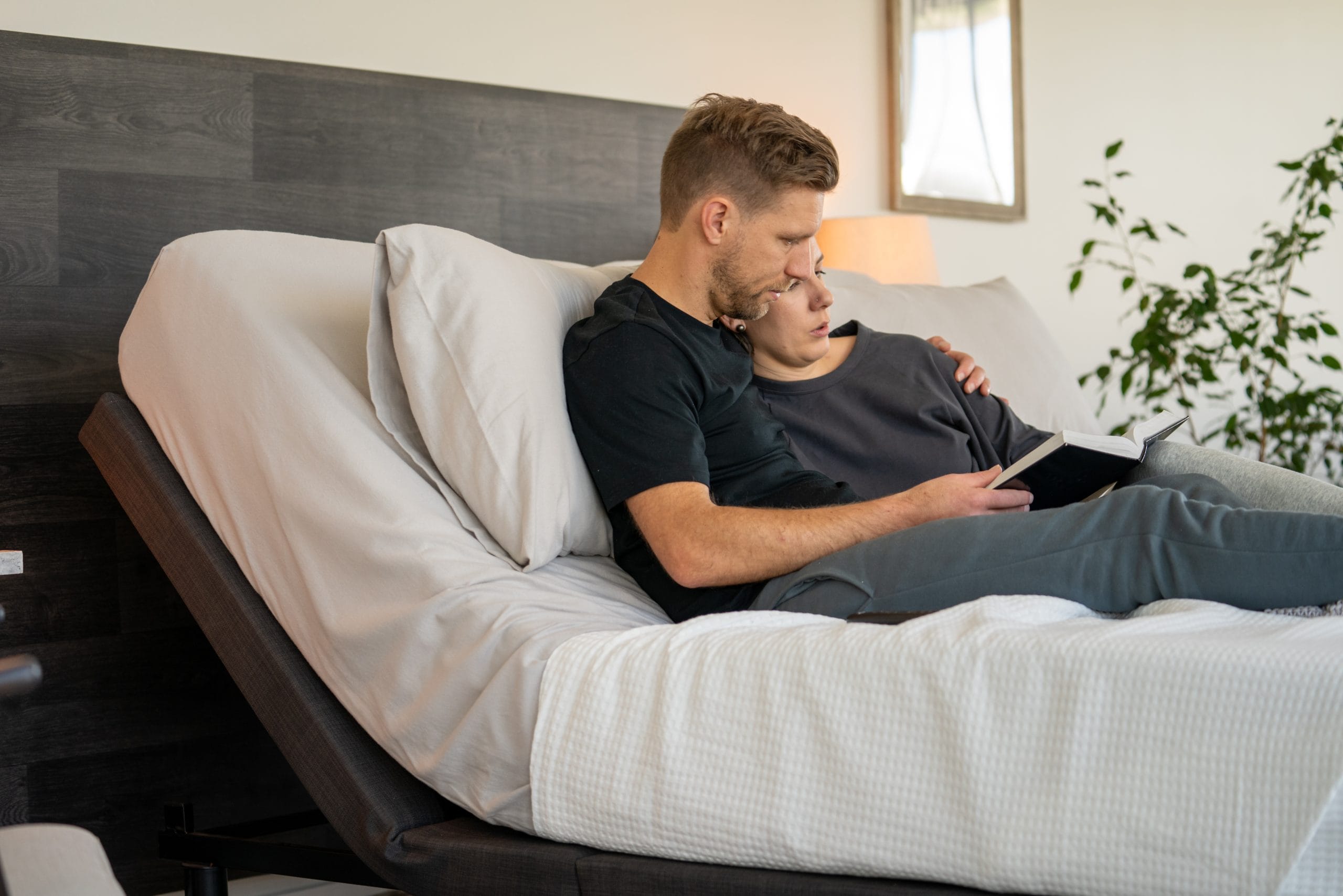 A couple relaxes together on an adjustable bed, with the head of the bed raised so they can sit up comfortably and read a book.