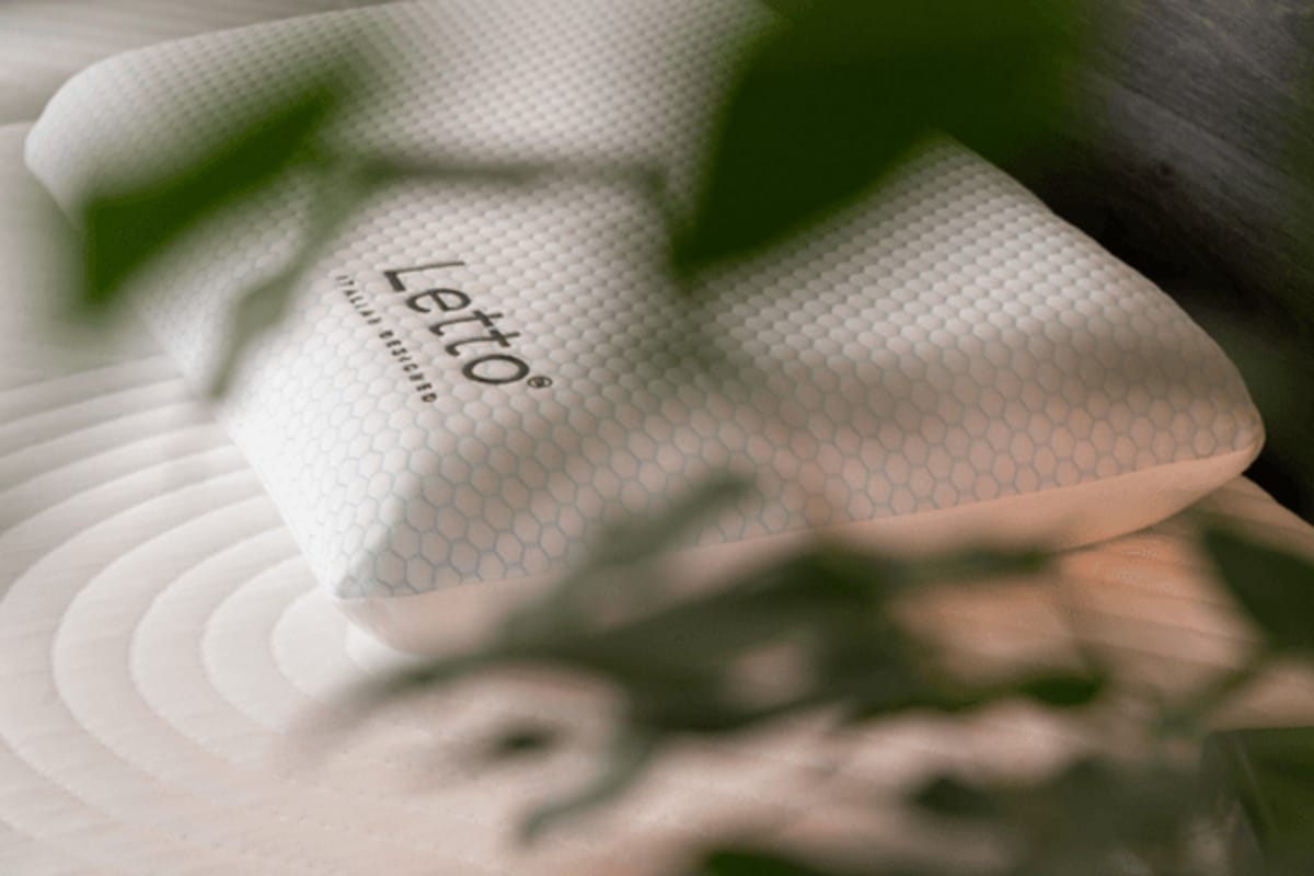 Close-up of a Letto-branded pillow with a hexagonal patterned cover, resting on a mattress with circular stitching design, partially framed by green leaves for a fresh and calming bedroom aesthetic.