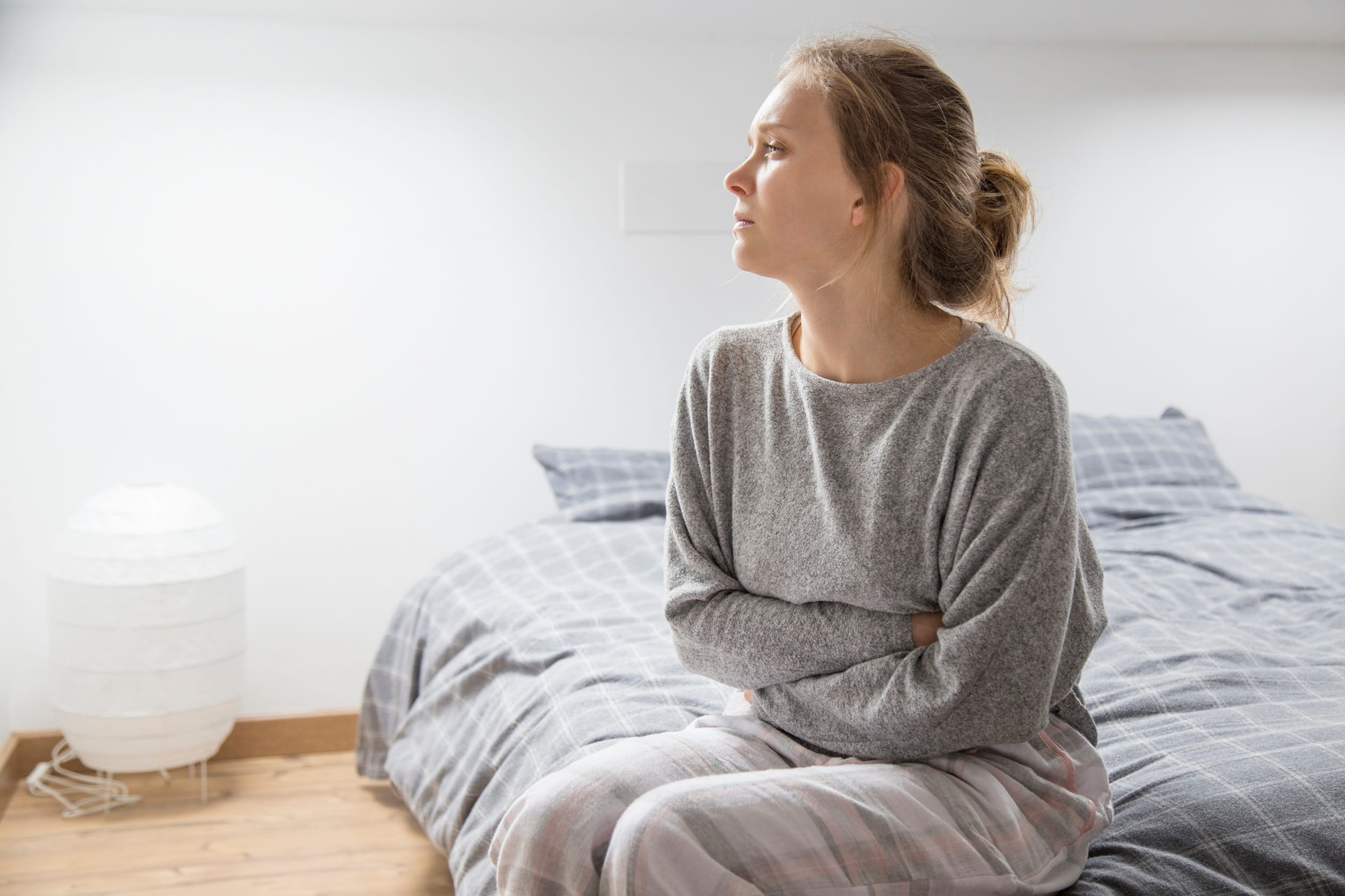 Woman sitting on the edge of the bed holding her stomach in discomfort from acid reflux symptoms