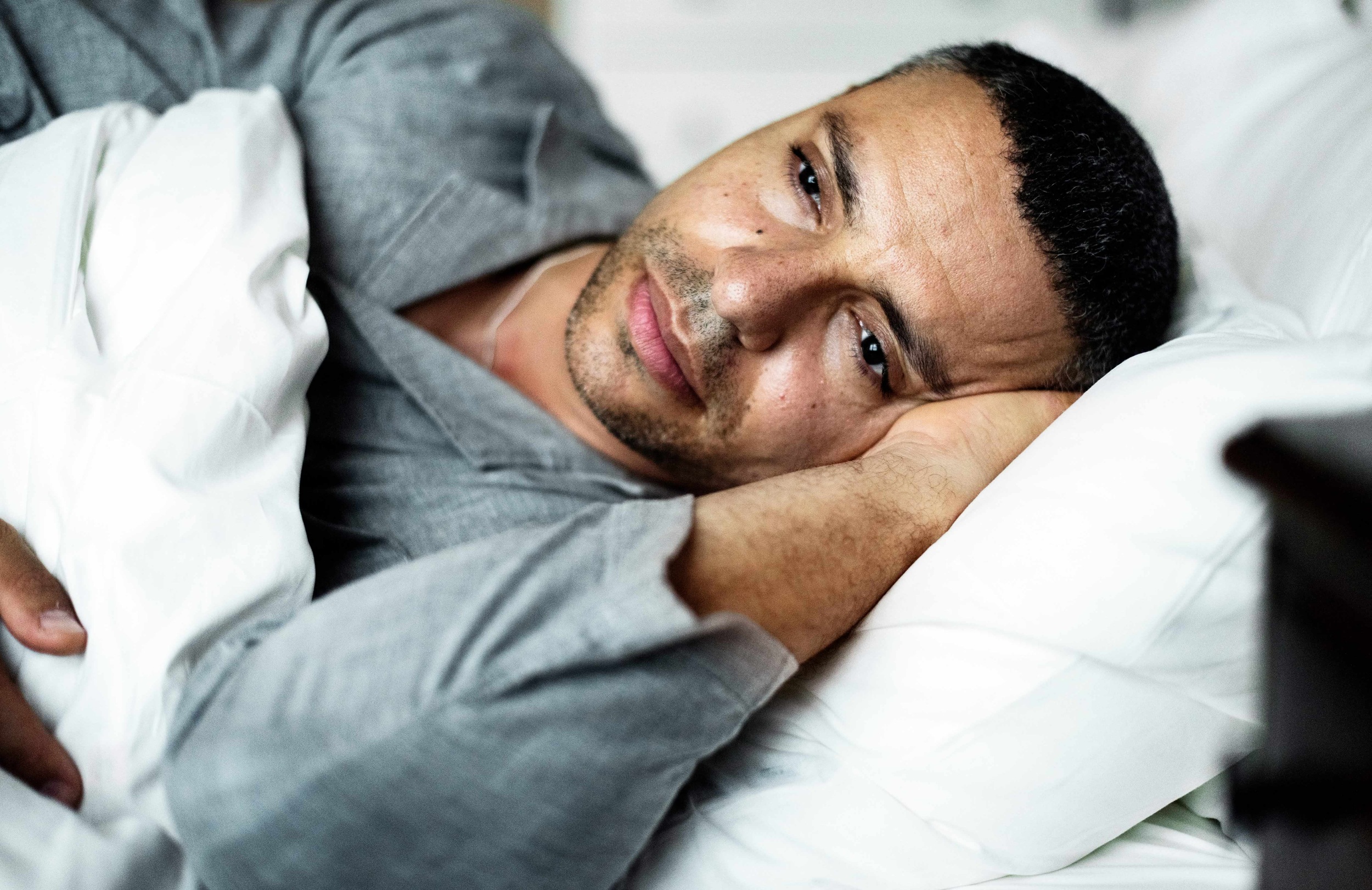 An awake man resting in bed looking thoughtful, representing the article's focus on the link between rest and mental health