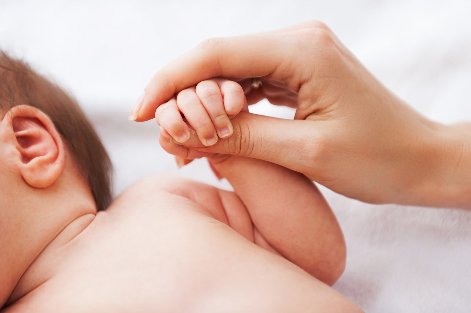 A close-up shot of a mother’s hand gently holding her newborn baby's tiny hand, symbolising the bond and the beginning of the postpartum recovery journey.