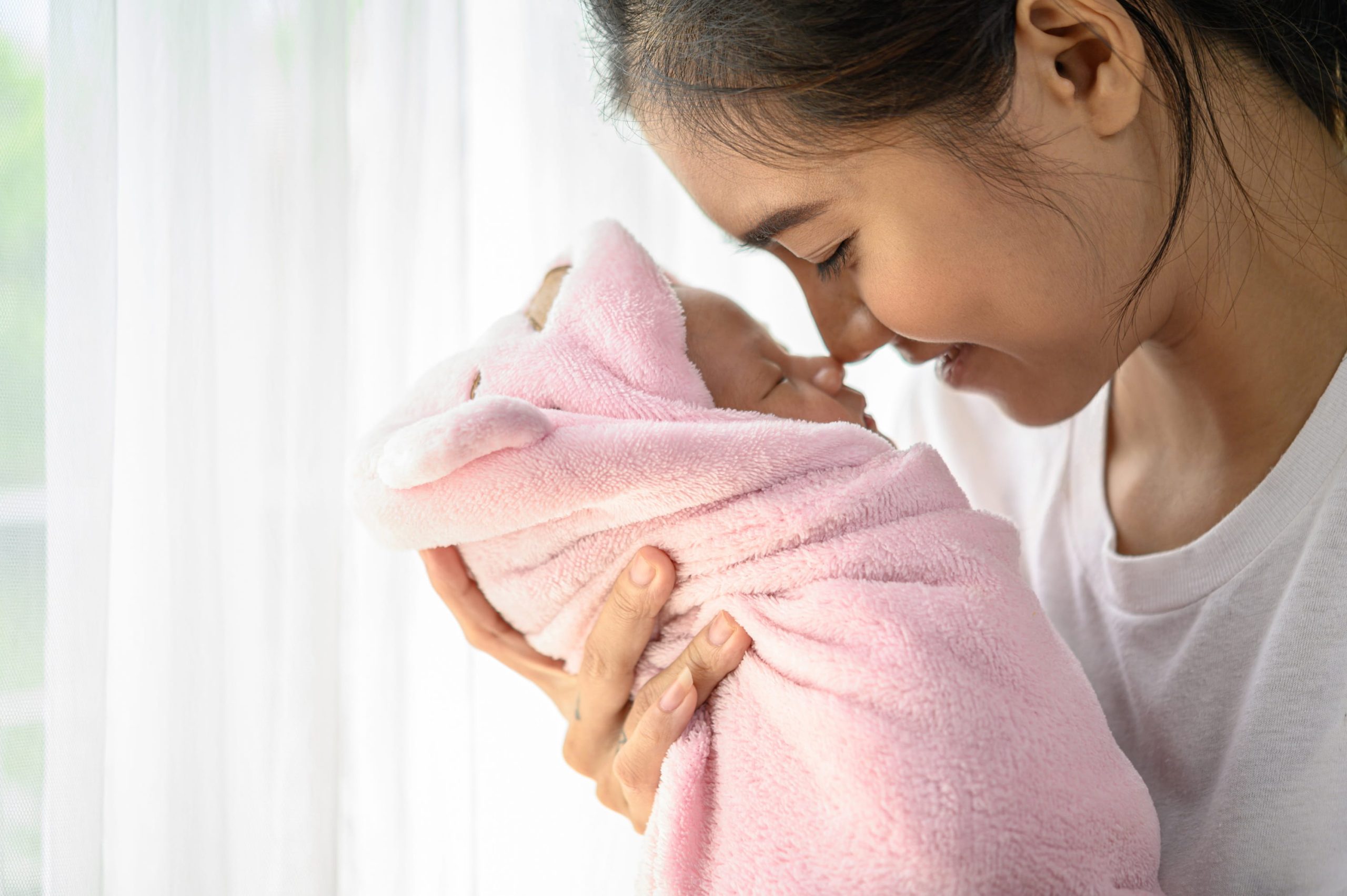 A smiling mother holding her swaddled newborn close to her face, reflecting the relief and peace that comes with finding comfort and support during the fourth trimester.
